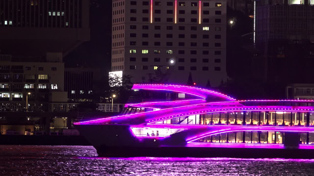 Victoria Harbour In Hong Kong With Purple Neon Light Ferry Sailing By At Night.