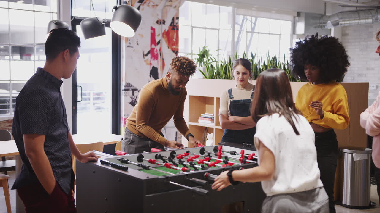 Young business creatives take a break playing table football at work