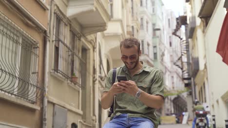 Young-man-sitting-on-city-street-and-looking-at-his-phone.