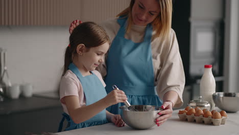 mom and daughter are cooking together in home kitchen little girl and her mother are mixing ingredients in bowl