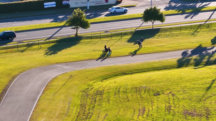 A group of kids ride bicycles along a sunlit path, casting long shadows on a vibrant green landscape