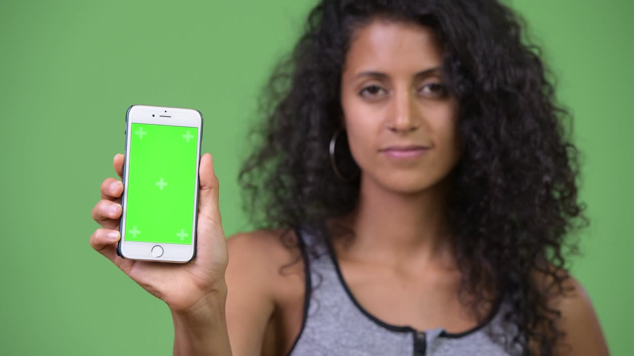 Young beautiful Hispanic woman with gym clothes showing phone