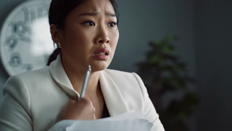 a woman appears worried as she clutches documents closely in a modern office. this moment conveys a sense of urgency and tension while a clock ticks in the background.