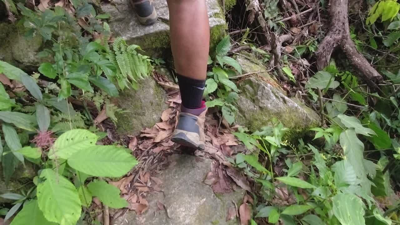 POV close-up follows woman's boots as she hikes up stony forest path