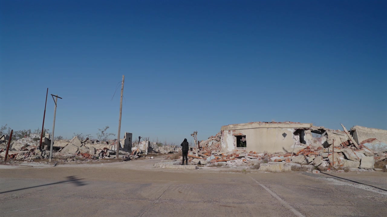 Ampia veduta di una persona in nero che sta in piedi tra alberi morti e desolati nelle rovine della città fantasma di Villa Epecuén, Argentina