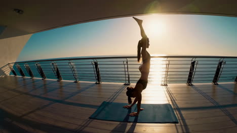 Woman performing a handstand yoga pose on a deck overlooking the ocean at sunset