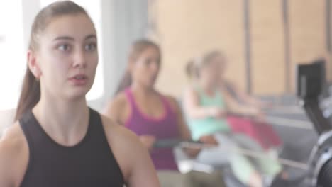 Focused-unaltered-diverse-women-exercising-on-rowing-machines-at-gym,-in-slow-motion