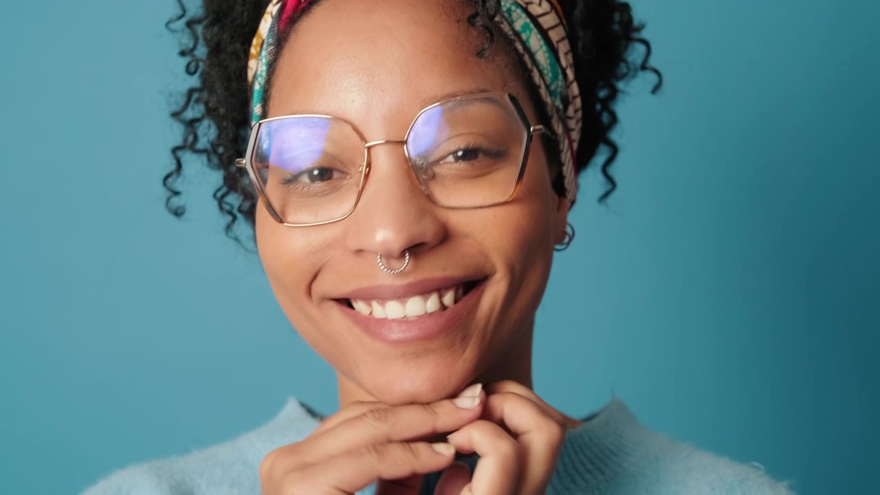 Smiling Young Woman with Glasses and Headband Posing Against Blue Background