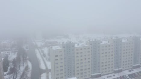 Schneebedecktes-Und-Nebliges-Drohnenvideo-Eines-Neunstöckigen-Gebäudes-Im-Sowjetischen-Stil-Mit-Vögeln-In-Einer-Stürmischen-Stadt