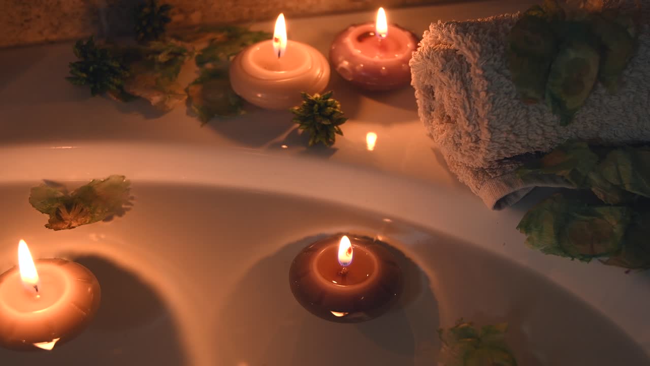 relajante fondo de spa con velas flotando en el agua del baño, algunos pétalos verdes y una toalla cerca de la superficie del agua