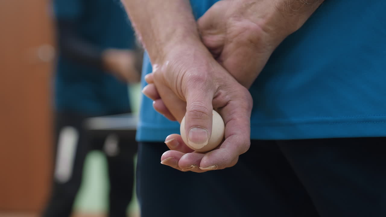 Detailed close up of senior coach hand holding table tennis ball behind back during practice session, emphasizing readiness, discipline, concentration, and preparation in indoor training