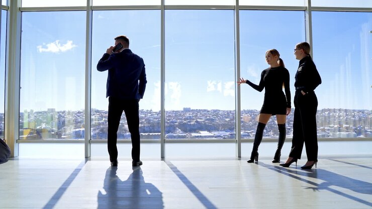 Handsome guy in suit and pretty women indoors. Businessman talking the phone. Young ladies flirting to a young man in office on windows background.