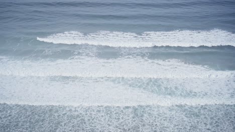 foamy ocean waves roll towards coastline, view from above