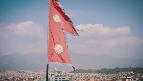 national flag of nepal flying against the blue sky and the kathmandu city on a sunny day. -wide shot