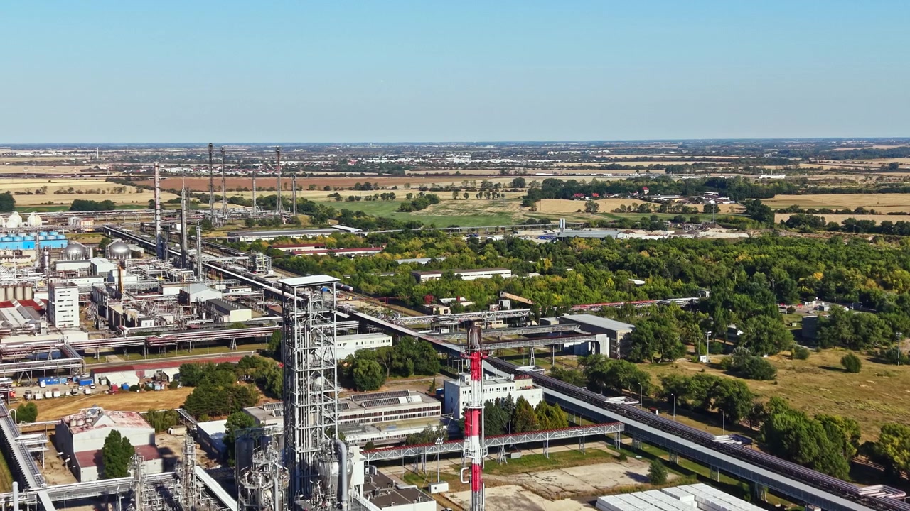 Industrial plant and landscape view with machinery, pipelines, and fields in the background during daylight