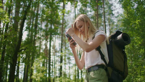 a traveler in the forest with a backpack walks along the path and looks at the mobile phone screen