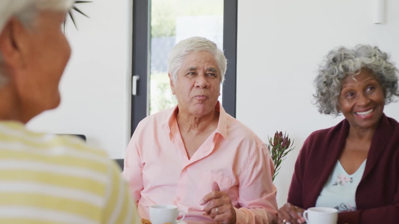 Personas mayores diversas y felices tomando té y conversando en un hogar de retiro.