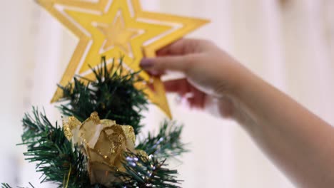 girl's hands putting star on top of christmas tree