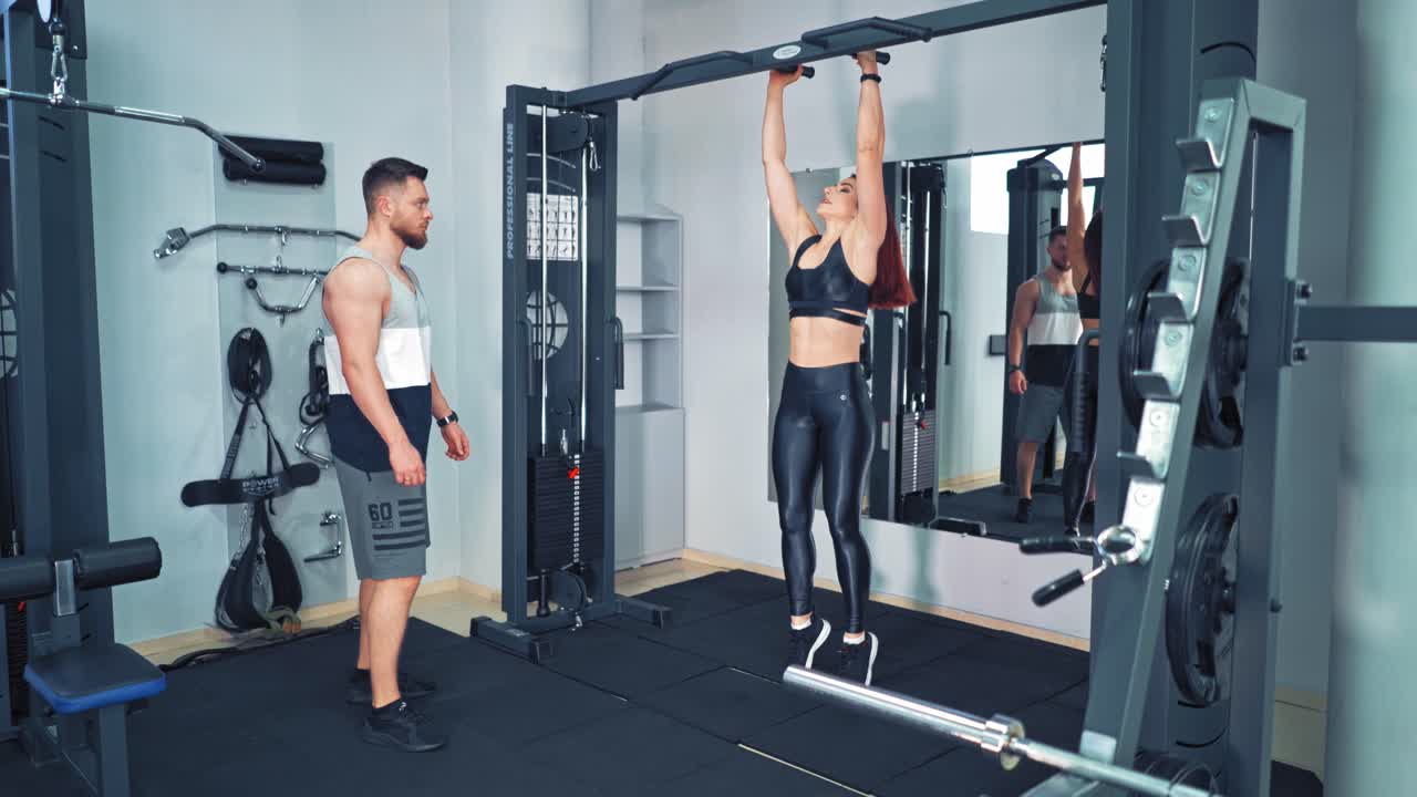 Couple training together in fitness center. Young beautiful woman doing exercises with personal trainer