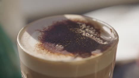 cappuccino-close-up-with-chocolate-power-on-top-on-a-green-desk-in-a-sunny-day