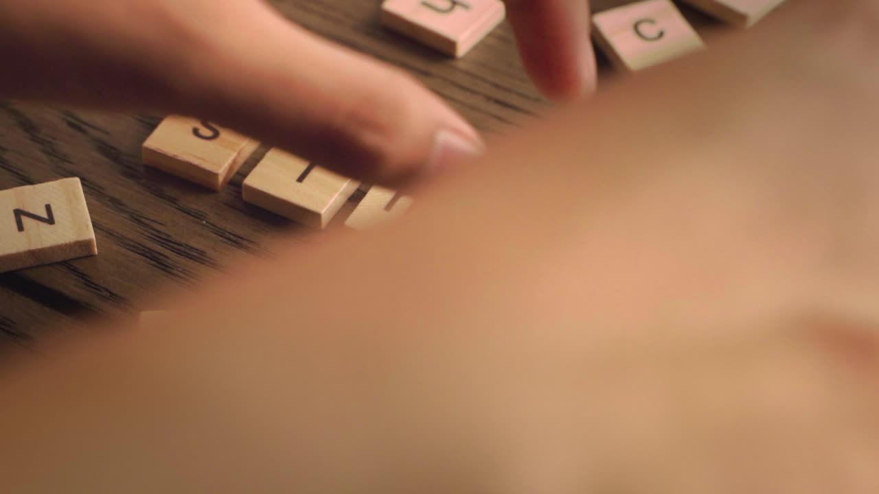 A hand carefully places wooden tiles to form the word simple on a rustic wooden surface.