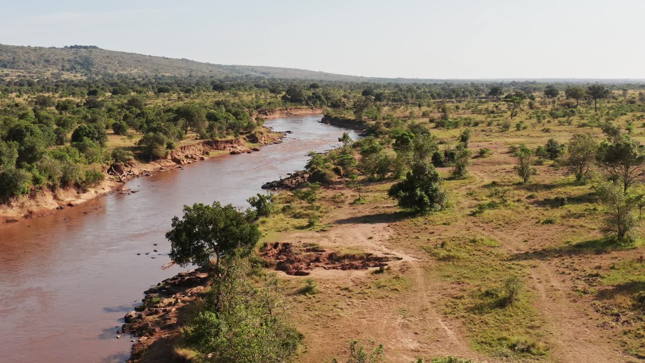 Tomada aérea de drone do cenário paisagístico do Rio Masai Mara, na África, Quênia, visto de cima, com belas árvores e vegetação exuberante, em um plano geral de estabelecimento amplo e elevado.