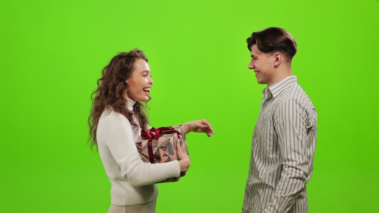 un hombre le está dando un regalo a una mujer. ella está muy feliz y sonríe. están abrazándose. están de pie sobre un fondo verde. pantalla verde. 4k.