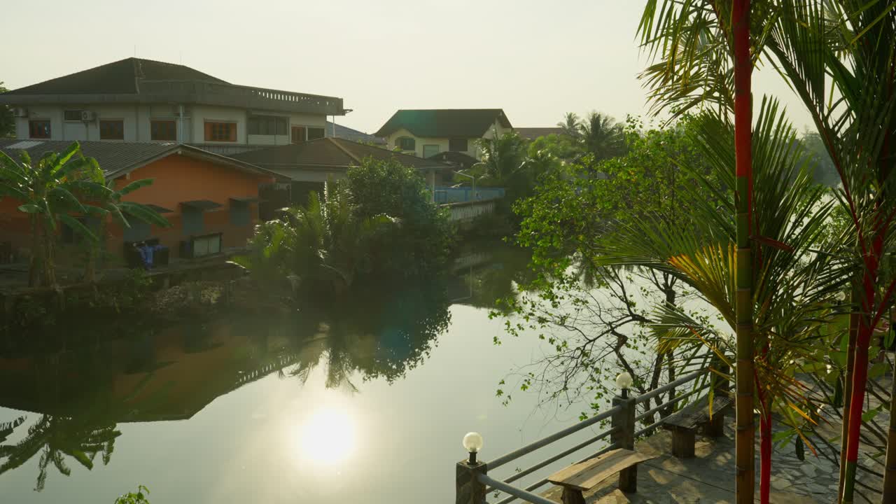 Sunrise over a calm canal with homes, trees, and golden reflections