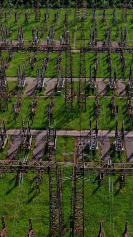 electric supports among green field.flight over huge field with high voltage steel pylons. high voltage lines in nature. aerial view. vertical video