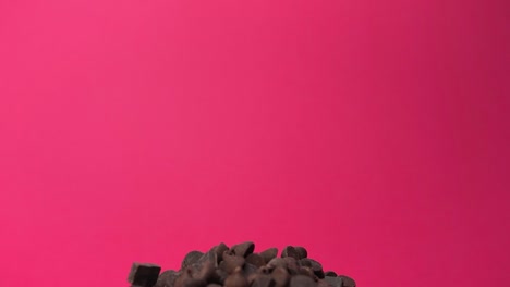 chocolate chips falling onto pile in slow motion with pink background close up macro