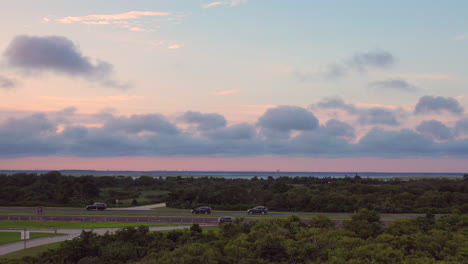 a low pan right as a car drives off into the sunset towards the right, with the sky - the horizon in view with pink and blue and yellow colors