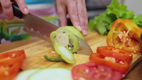 manos femeninas de la ama de casa con un cuchillo cortado pimienta fresca en la mesa de la cocina de la mesa de corte