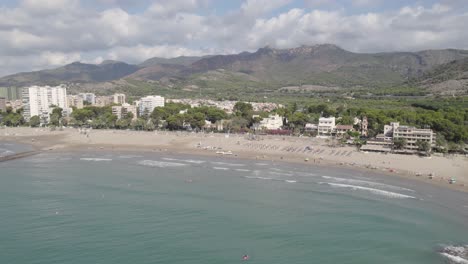 Seitliche-Luftaufnahme-Des-Voramar-Hotels-Und-Strandes-In-Benicassim-An-Einem-Sonnigen-Tag-Mit-Den-Bergen-Der-Wüste-De-Les-Palmes-Im-Hintergrund,-Spanien