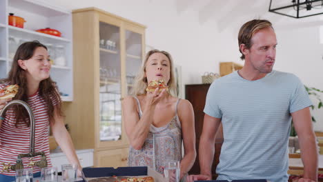 familia de varias generaciones alrededor de la isla de la cocina comiendo pizza para llevar juntos