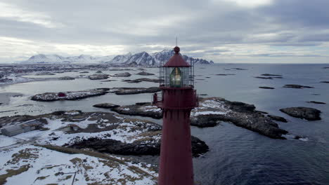 Hermoso-Pedestal-Aéreo-Del-Faro-De-Andenes-En-Noruega-Con-La-Costa-Rocosa-Moteada-De-Nieve-Y-Las-Montañas-En-El-Fondo