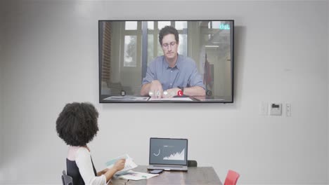 mujer de negocios afroamericana en videollamada con un colega caucásico en la pantalla de televisión