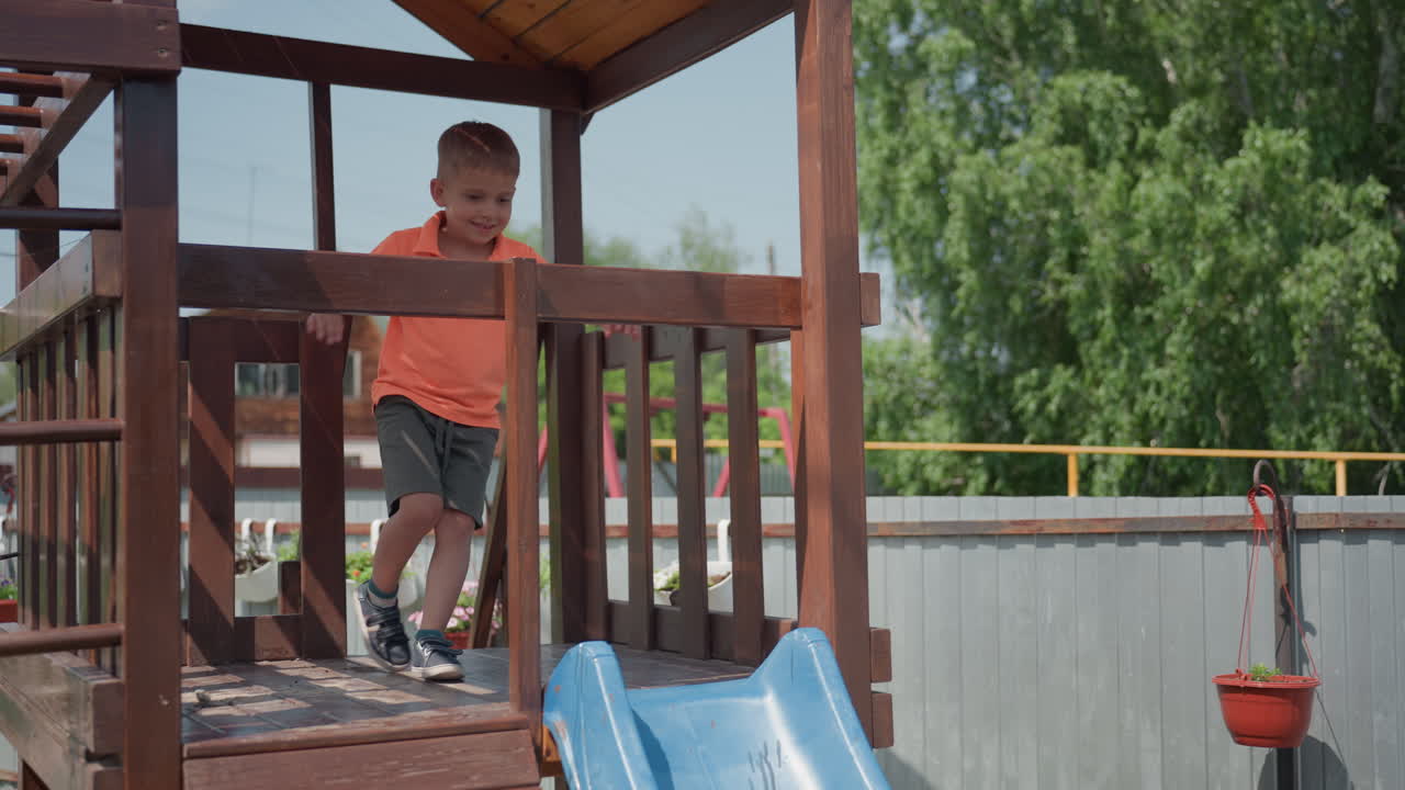 Child Slides Down, Caucasian Toddler Descending Slide Happily, Little Boy With Bright Shirt Climbs And Glides Down Slide, Young Child In Orange Shirt Explores And Enjoys Sunny Playground Adventure