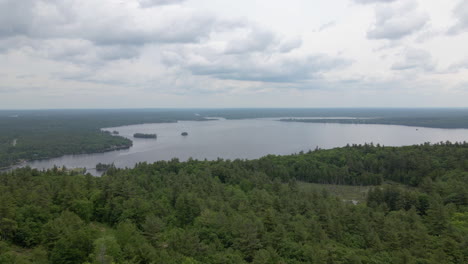 Aerial shot over green tree covered mountain on to large lake on cloudy day. Calabogie Ski hill. Ontario Canada