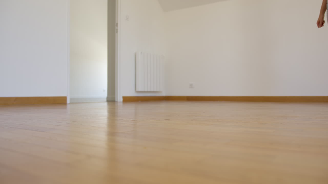 Young woman walking on empty wooden apartment floor, low angle view