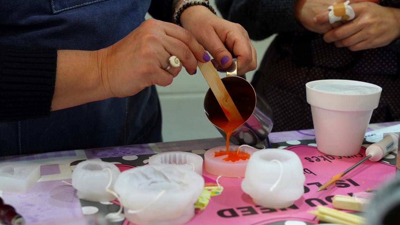 Un ceraiolo creativo versa cera liquida colorata in uno stampo in silicone durante un laboratorio artigianale.
