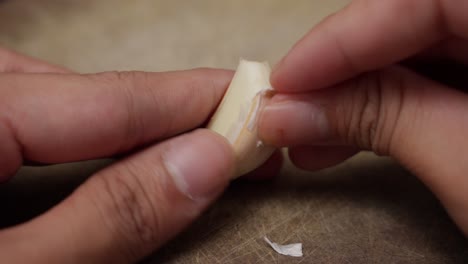 person peeling garlic clove carefully with fingers on a textured cutting board in kitchen setting