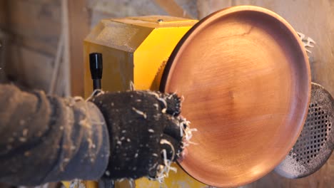 carpenter in sawdust inspects product at lathe.