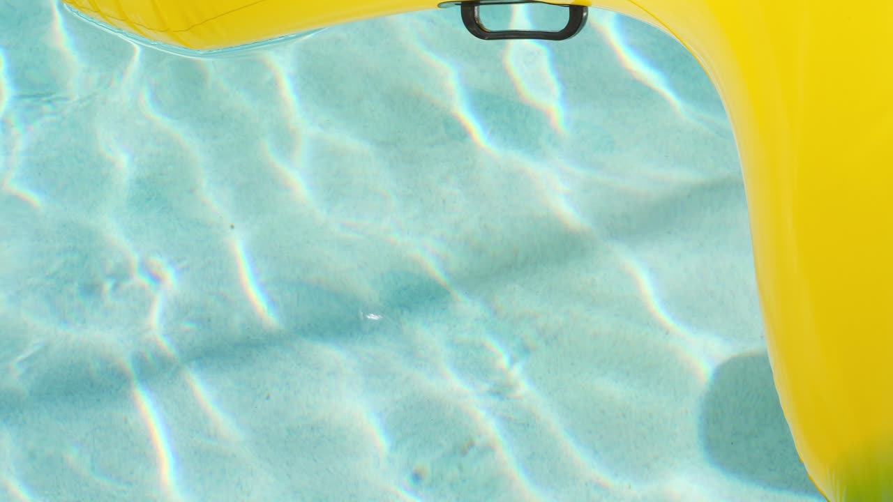 Beautiful ripples dance on the floor of a sunny pool while a yellow pool floaty moves around the edge of the frame in slow motion.