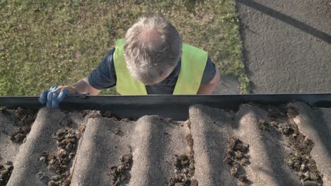 older male with high vis on cleans roof gutter and walks away from task