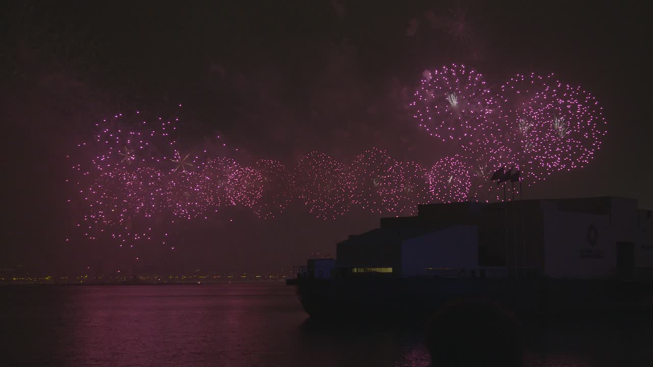 대규모의 불꽃놀이가 바물 위에 빛나고 있으며, 해안가에 있는 msheireb 박물관의 실루이 있습니다.