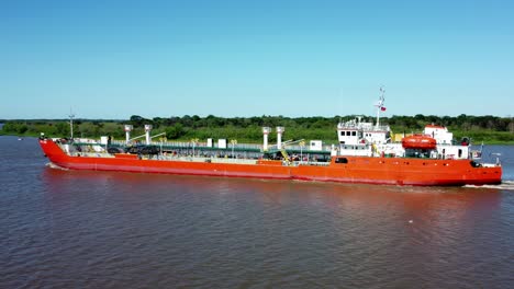 side shot of huge long red commercial ship crossing narrow arm of river, paraguay