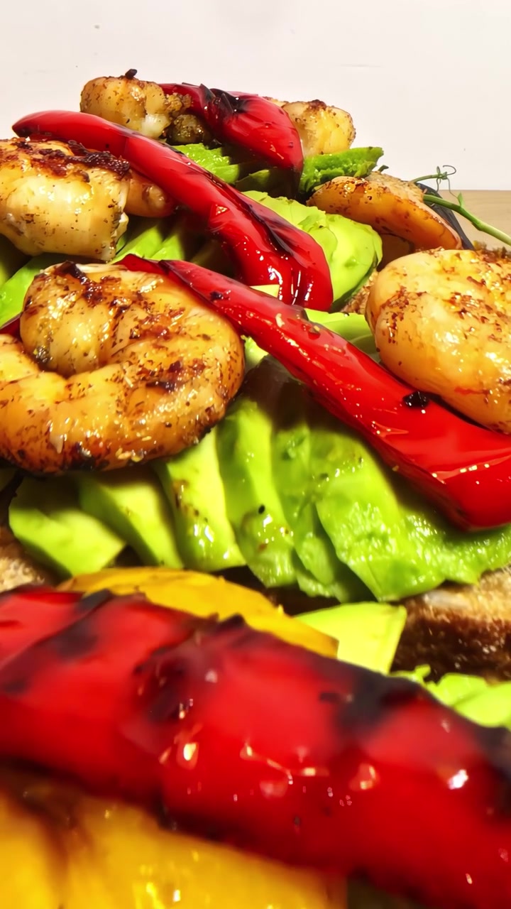 Gamberi scottati con avocado a fette e peperoni rossi arrostiti glassati su crostino, primo piano ravvicinato.