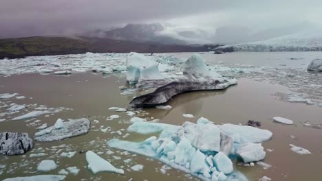 Fly-in-between-two-iceberg-peaks-floating-in-a-muddy-glacier-lagoon-in-Iceland