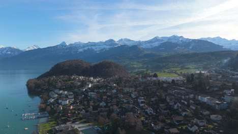 Spiez-on-Lake-Thun-with-Swiss-Alps-backdrop,-clear-sky,-aerial-view