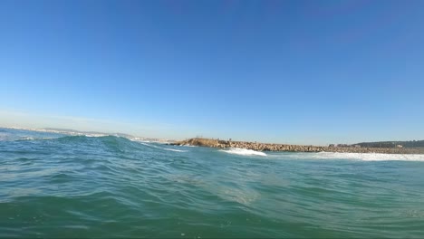 Blaue-Meereswelle-Am-Strand-Von-Caparica-Mit-Fischer-Im-Hintergrund